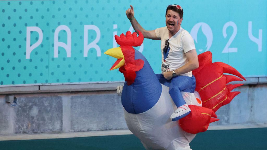 A man wears a costume that appears to show him riding atop an inflatable cockerel