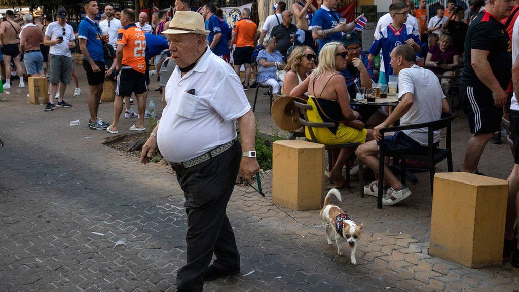 A man walks his dog in front of Rangers fans