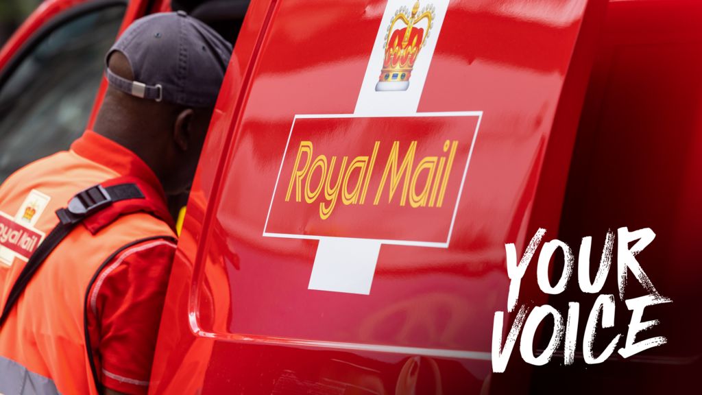A Royal Mail poste dressed in a orange high-vis vest and red polo and navy blue cap looks into his Royal Mail work van side door