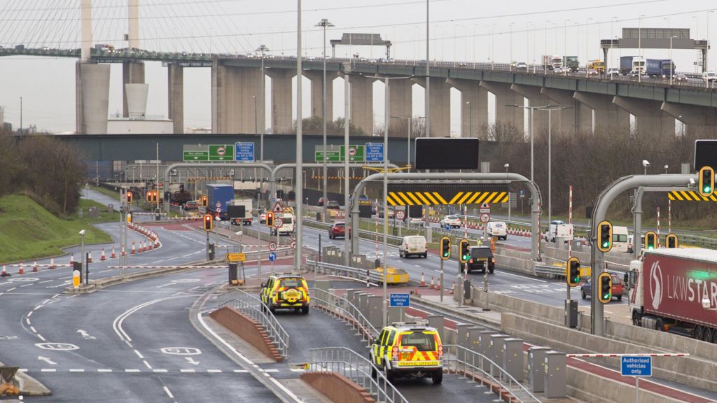 An overhead view of traffic waiting to join one of the bore tunnels at the Dartford Crossing. In the background is the Queen Elizabeth II Bridge.