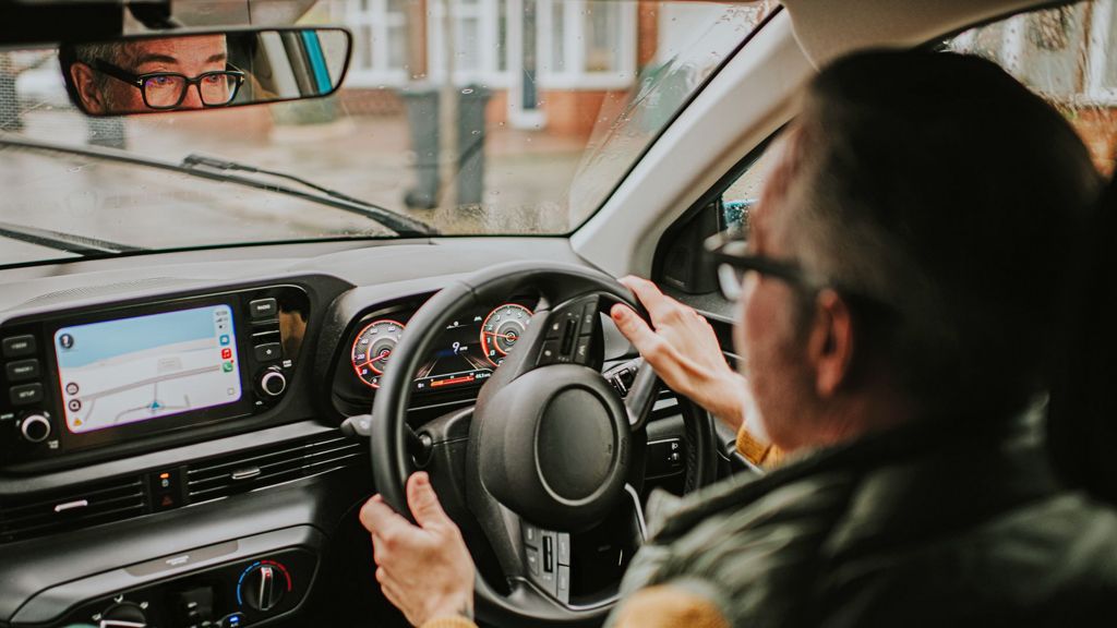 View over the shoulder of a male  driver. He has is wearing glasses. It is a rainy day