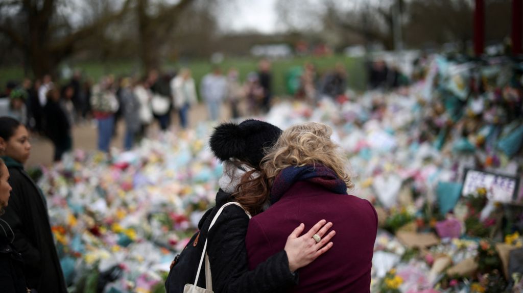 People observe a memorial site at the Clapham Common Bandstand,