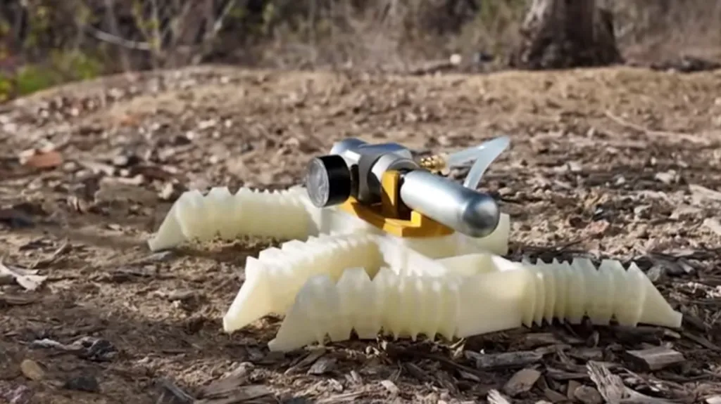 A small, six-legged robot crawls across the ground. It has a cylinder on its back