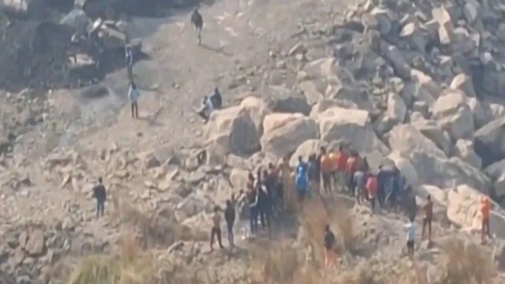 A view of the mine blast site. Large boulders in a hilly area and gatherings of men can be seen