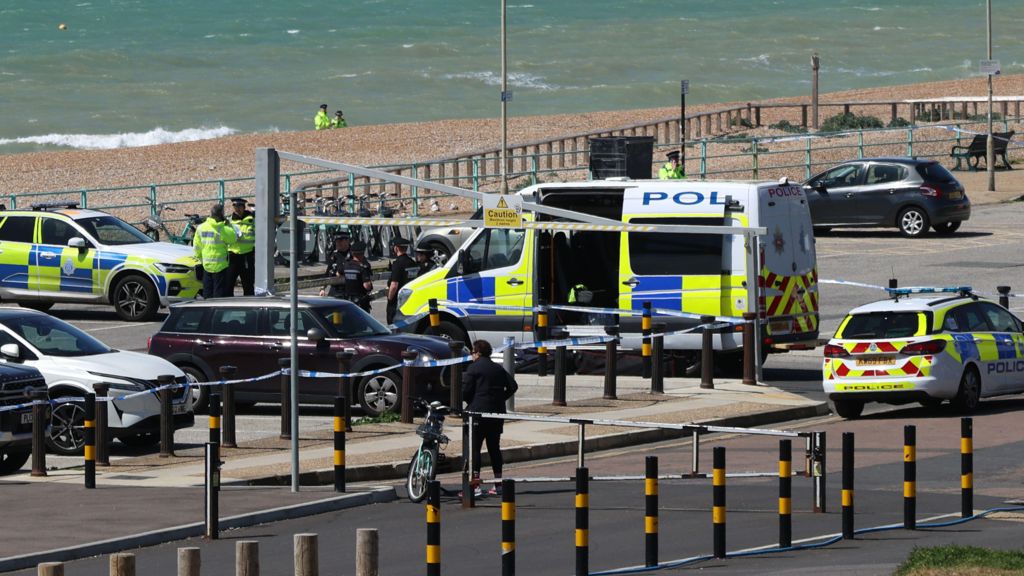 Police vehicles and officers in the Black Rock car park on Madeira Drive after the bodies of three women were recovered from the sea in Brighton. The car park is next to a pebble beach, where two more officers are standing in the distance
