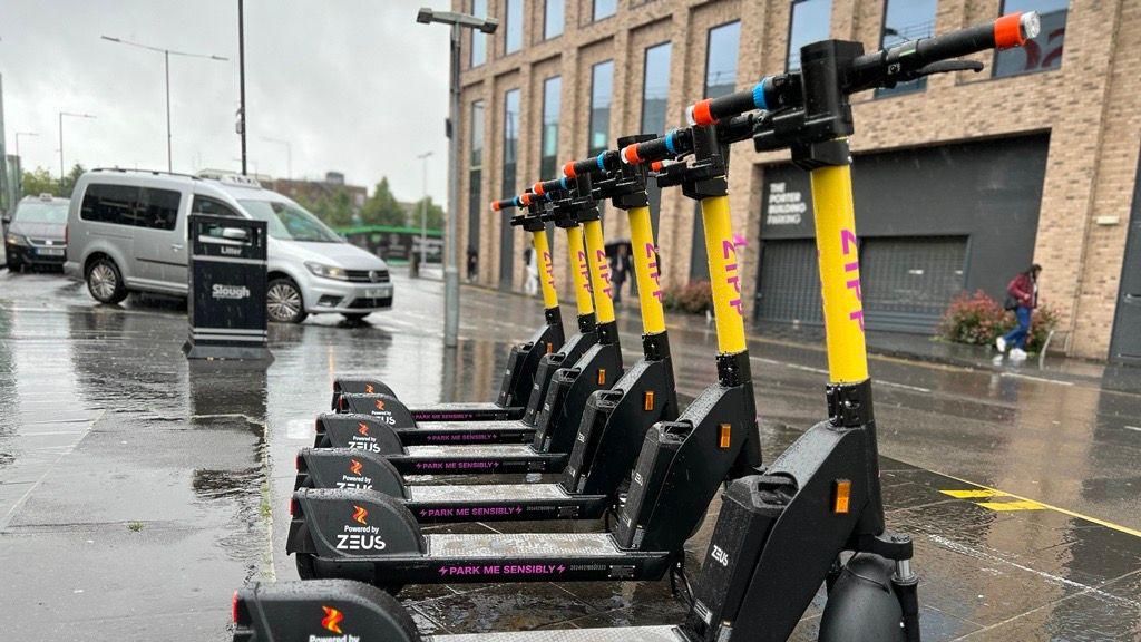 A row of yellow scooters with a rainy street and people walking