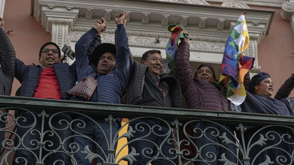 President Luis Arce stands holding hands with people on a balcony