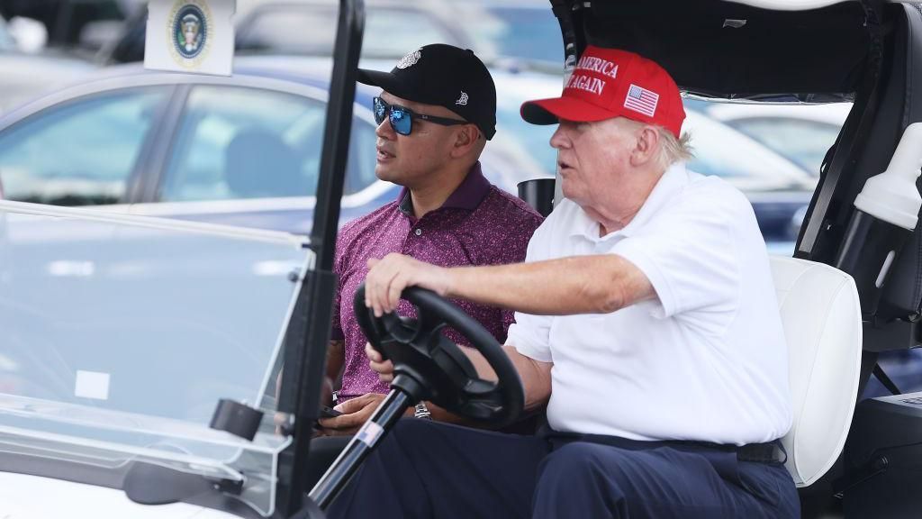  Donald Trump drives a golf cart accompanied by aide Walt Nauta