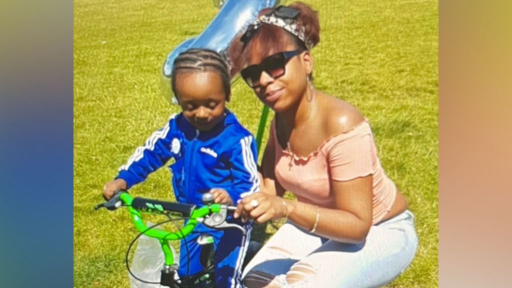 Boy in blue Adidas tracksuit on a green handlebarred bike with a woman in jeans and peach top wearing sunglasses