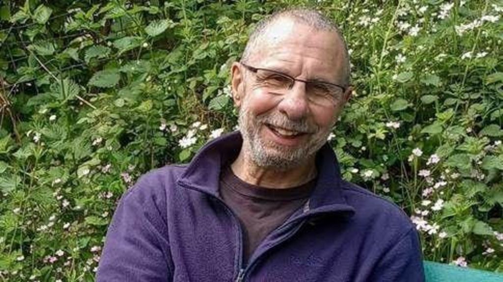 James "Jim" O'Neill, in a dark coloured t-shirt and blue fleece jumper, wearing glasses and smiling at the camera.