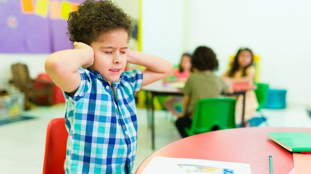 Stock photo of young boy covering his ears in a classroom