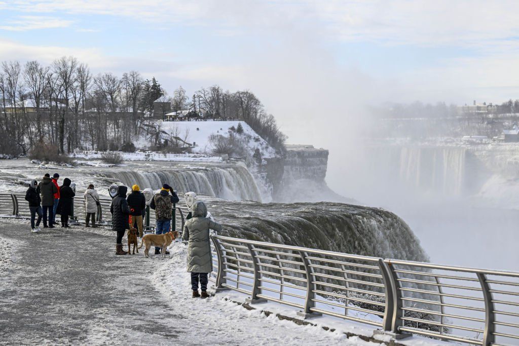 Туристы стоят у забора, глядя на водопад