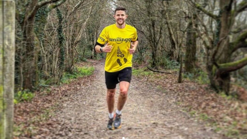 Man running through a woodland smiling 