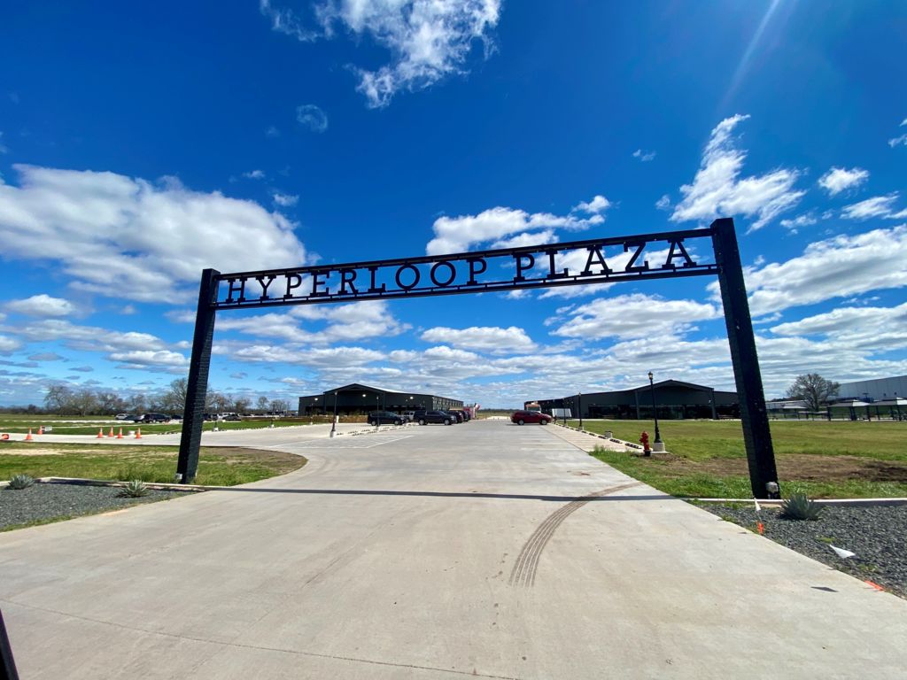 A sign reads "Hyperloop Plaza" and a road leads to a parking lot with a few buildings beyond in the distance
