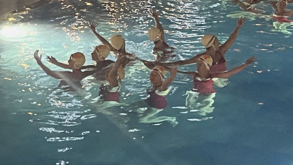 A group of synchronised swimmers with their arms in the air