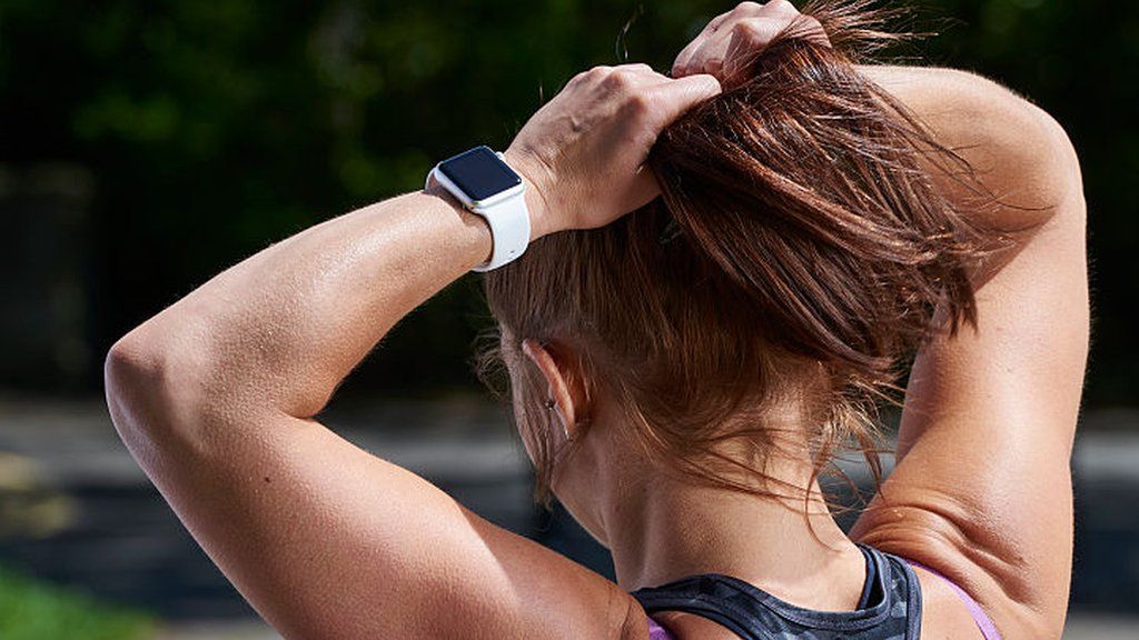 Detail of a woman in sportswear tying back her hair while modelling an Apple Watch Sport