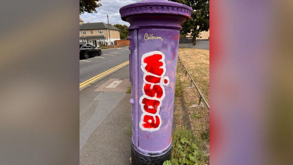 A Royal Mail postbox is painted purple with the word wispa written down the side in red paint.