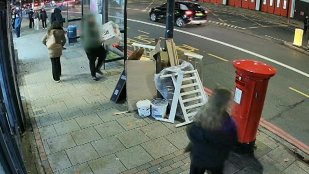 CCTV still of a blurred person putting a large cardboard box on to a large pile of household wate next to a bus stop