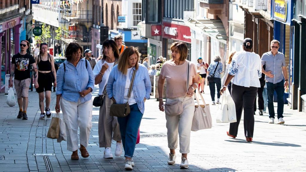People carrying shopping bags and walking through a shopping street in Shrewsbury  on a sunny spring day