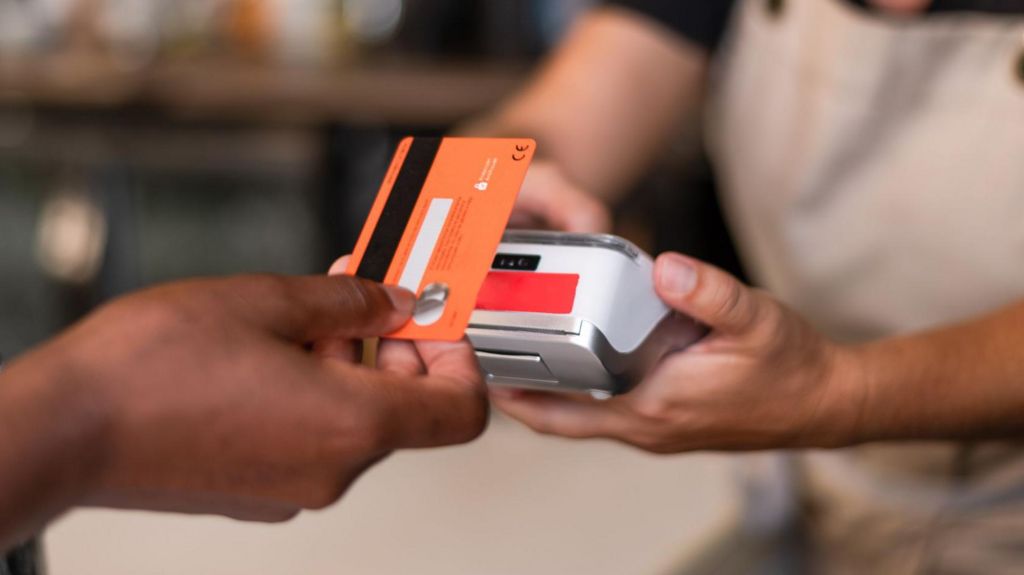 Contactless card payment being made with a card held in a hand and a terminal being held by someone in an apron.