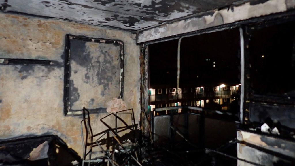 A room damaged by fire, showing walls, chairs and a window covered in soot.