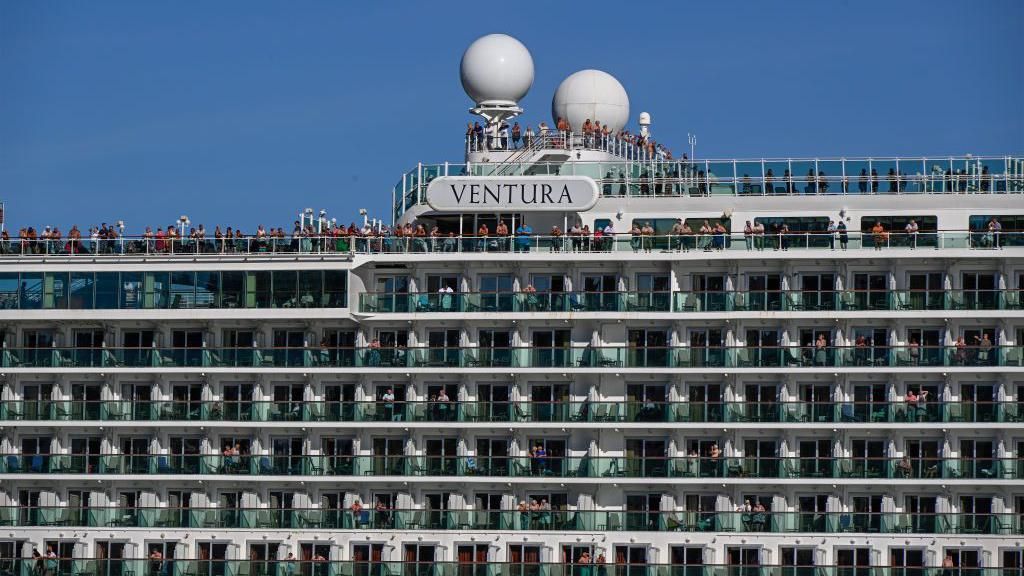 Passengers stand on deck next to Ventura sign