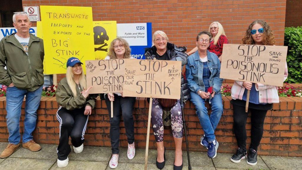 Seven people sat on a wall all holding placards with the words 'Stop the Stink'