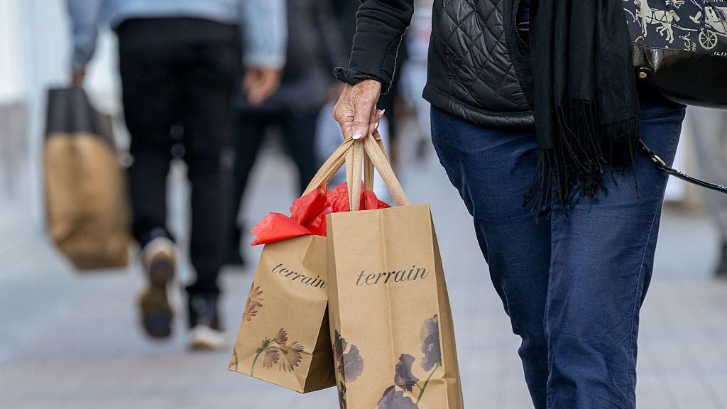 Cropped shot of the bottom half of a shopper wearing jeans and carrying two brown paper Terrain bags at Broadway Plaza in Walnut Creek, California, US, on Thursday, Dec. 11, 2025.