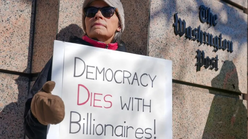 A woman holds a placard outside The Washington Post, with the a sign of the newspaper in the background