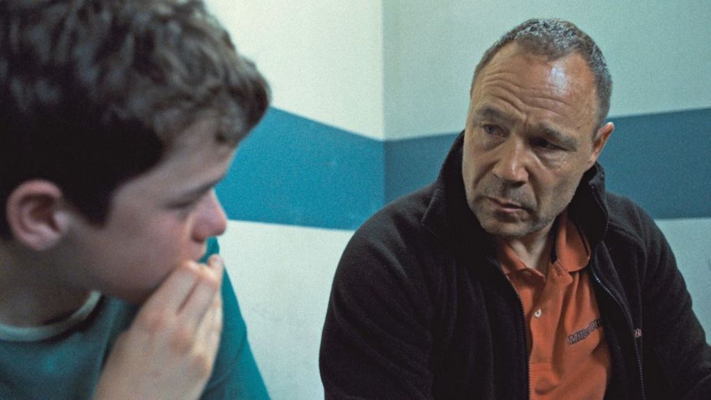 Owen Cooper and Stephen Graham looking at each other in a police interview room in a scene from Adolescence