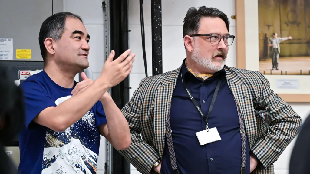 Composer Dai Fujikura and librettist Harry Ross. Dai is wearing a navy blue T shirt with Hokusai's The Great Wave printed on the front. Harry is wearing a navy blue shirt with a checked suit jacket. He has glasses.