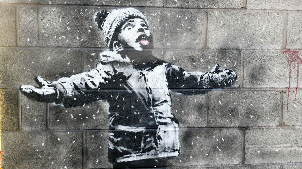 A lack and white mural of a small boy wearing a woolly hat, looking up with his mouth open, catching snowflakes