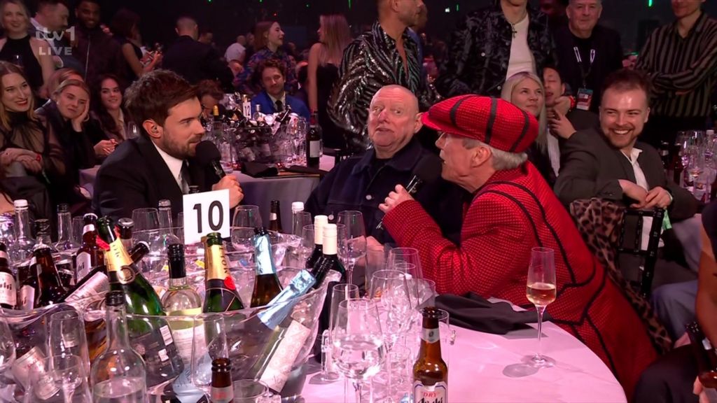 Jack Whitehall interviews Shaun Ryder and Bez at their table.