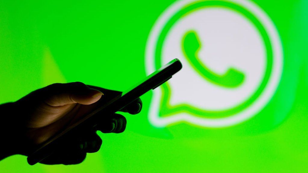 Person holds a smartphone against a WhatsApp logo background