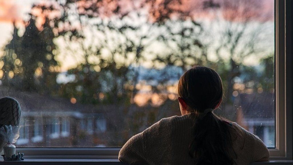 A girl looks out of a window at a sunset