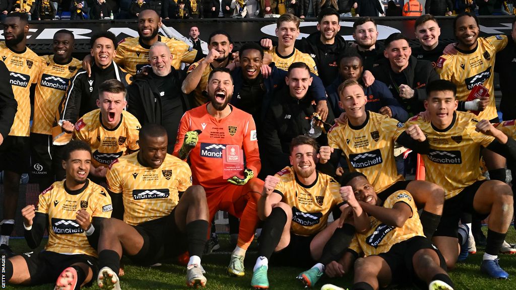 Sam Bone, sat down to the right of goalkeeper Lucas Covolan, on the pitch with his Maidstone United team-mates after the non-league side beat Ipswich Town in the fourth round at Portman Road