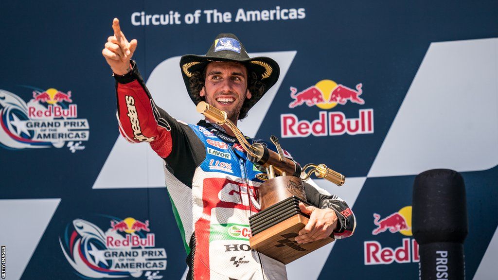 Alex Rins points while holding the trophy on the podium after winning the Grand Prix of the Americas