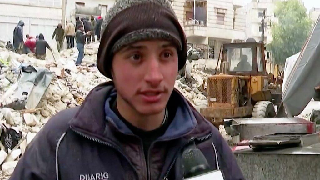 Young man speaks in front of pile of rubble in Aleppo, Syria