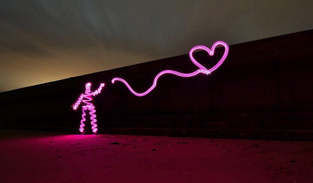 Pink light painting character holding a heart on the end of a string on Frinton-on-Sea beach in Essex