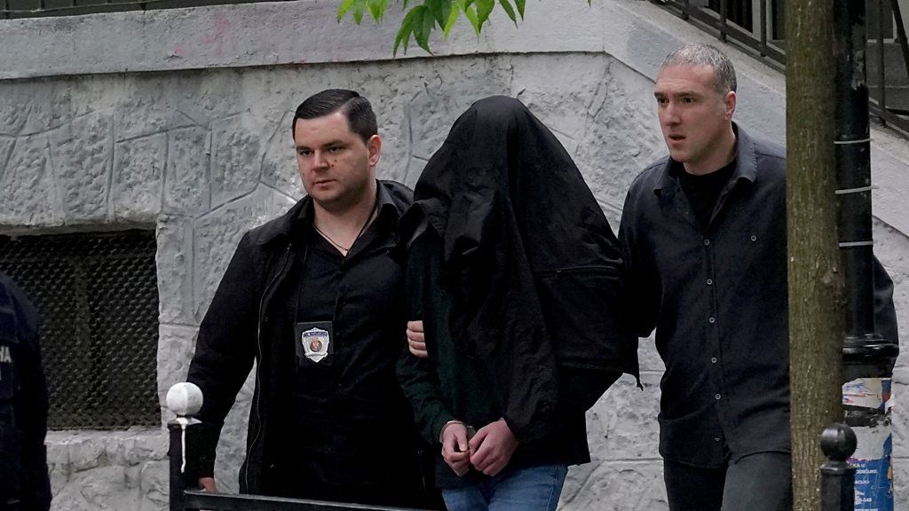 Police escort suspect whose face is covered by a black jacket in Belgrade