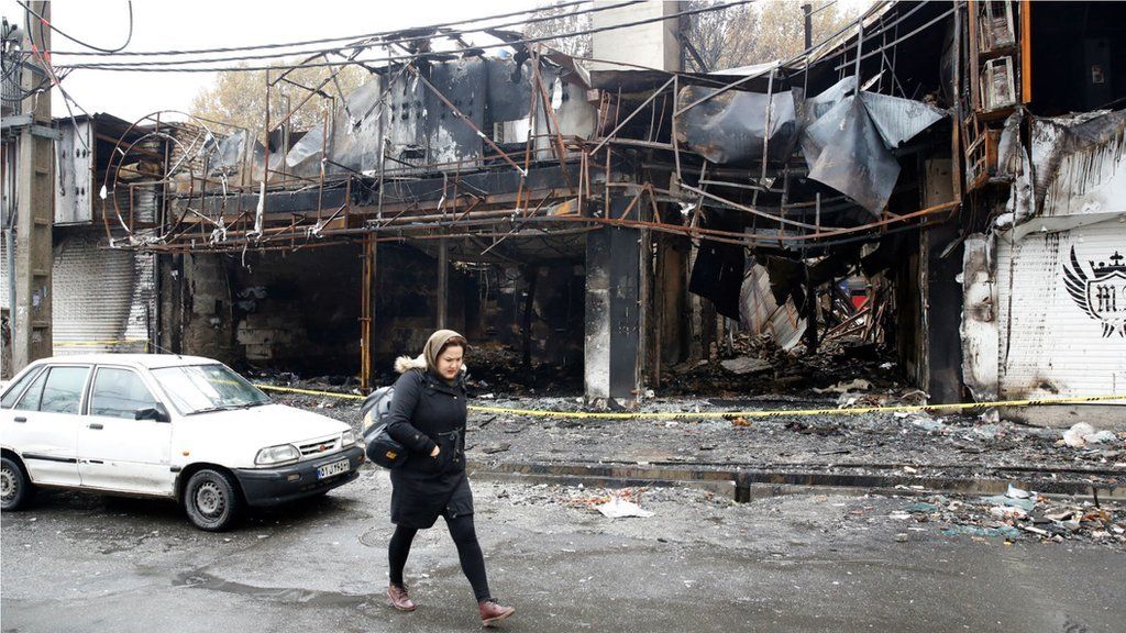 An Iranian woman walks past a shopping centre that was burned during protests over increasing fuel prices in the city of Shahriar, Alborz province, Iran, 20 November 2019.