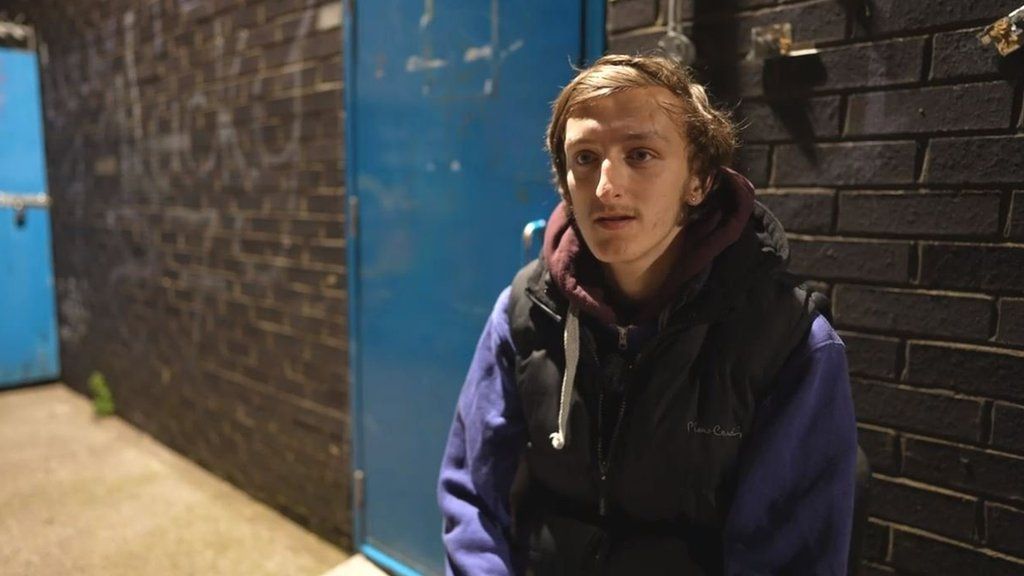 Samuel Atkinson sitting extracurricular  a stateless  shelter. He is wearing a purple jumper and achromatic  gilet.