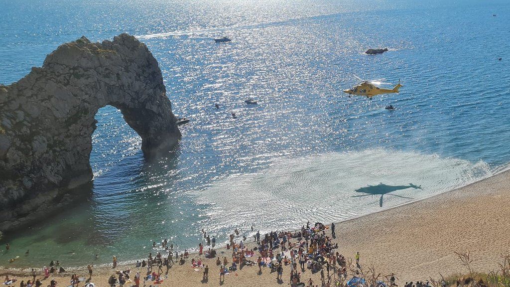 Air ambulance taking off from Durdle Door beach with Durdle Door sea arch in the background