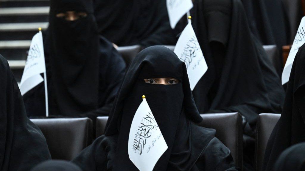 A veiled woman holiding a Taliban flag attends a pro-Taliban event at a Kabul university.
