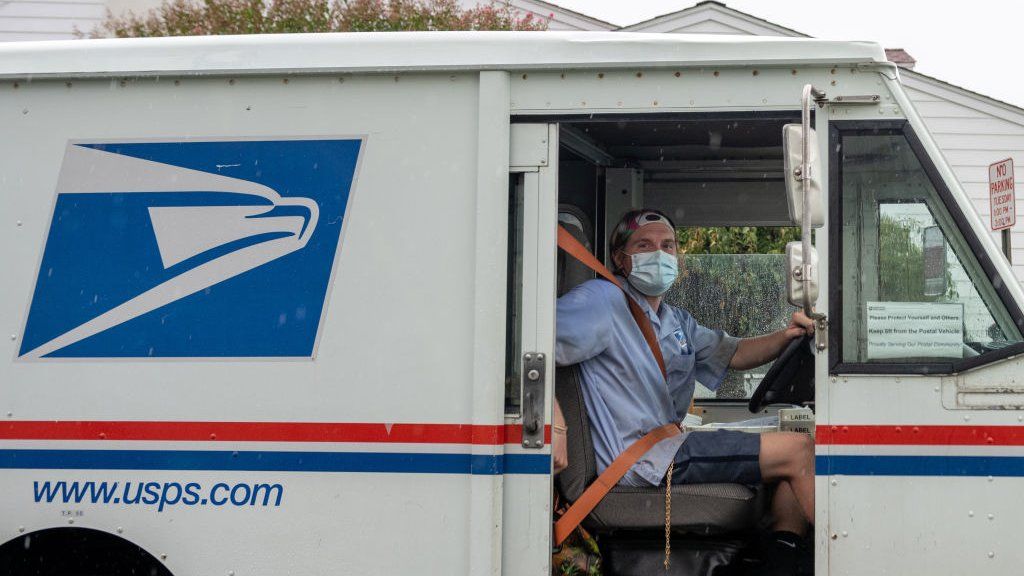 A postal worker delivers mail wearing a mask