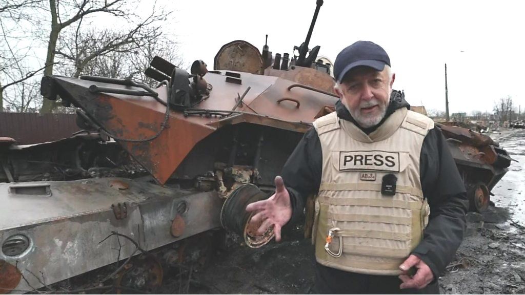 The BBC's Jeremy Bowen in front of armoured vehicle wreckage