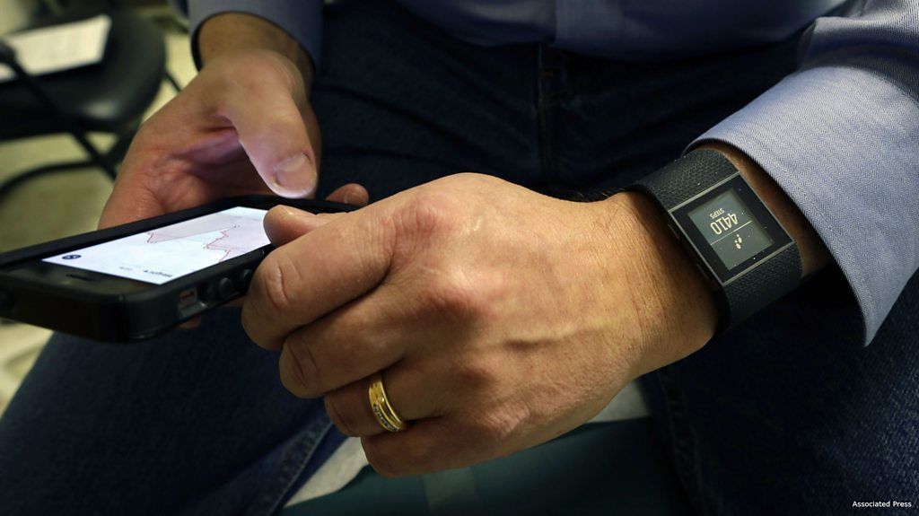 Man wears FitBit watch and uses mobile phone.