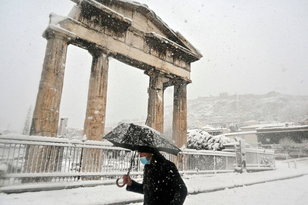 Мужчина держит зонтик в снегу возле Римской Агоры в центре Афин