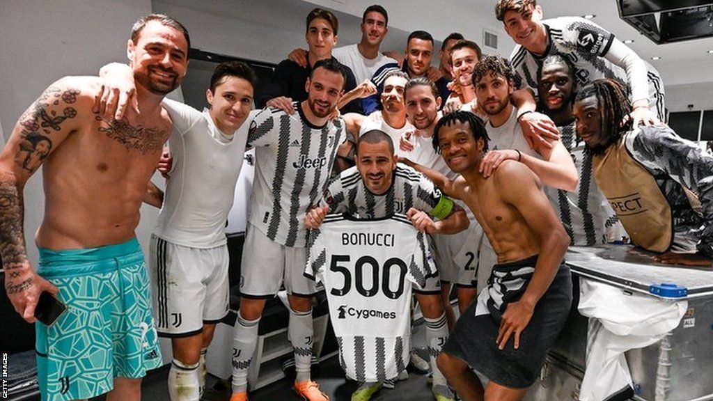 Leonardo Bonucci holding a Juve shirt with 'Bonucci 500' on the back alongside his team-mates in the dressing room