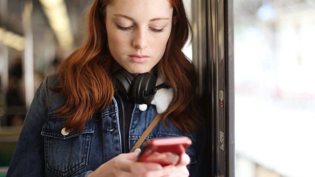 A young woman with red hair holding a phone in a railway carriage (stock photo)